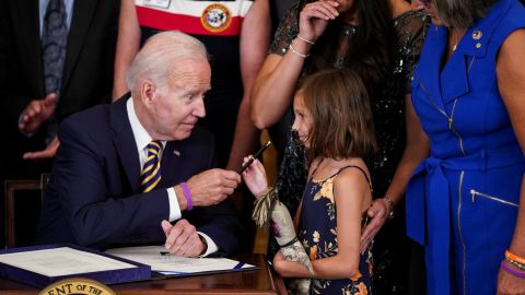 US President Joe Biden hands the pen of Brill Robinson, daughter of Sgt.  First Class Heath Robinson, where her mother Danielle Robinson stands during a signing ceremony 