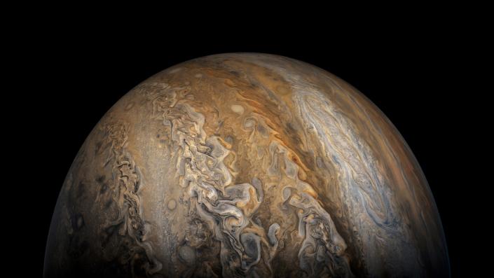 Jupiter rises in the dark with bands of orange, white, and purple-brown