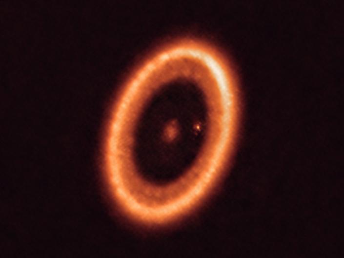 The image shows an orange star surrounded by an orange disk of material with a small dotted planet